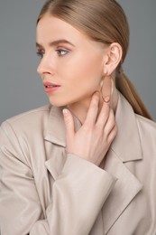 Beautiful young woman with elegant earrings on gray background