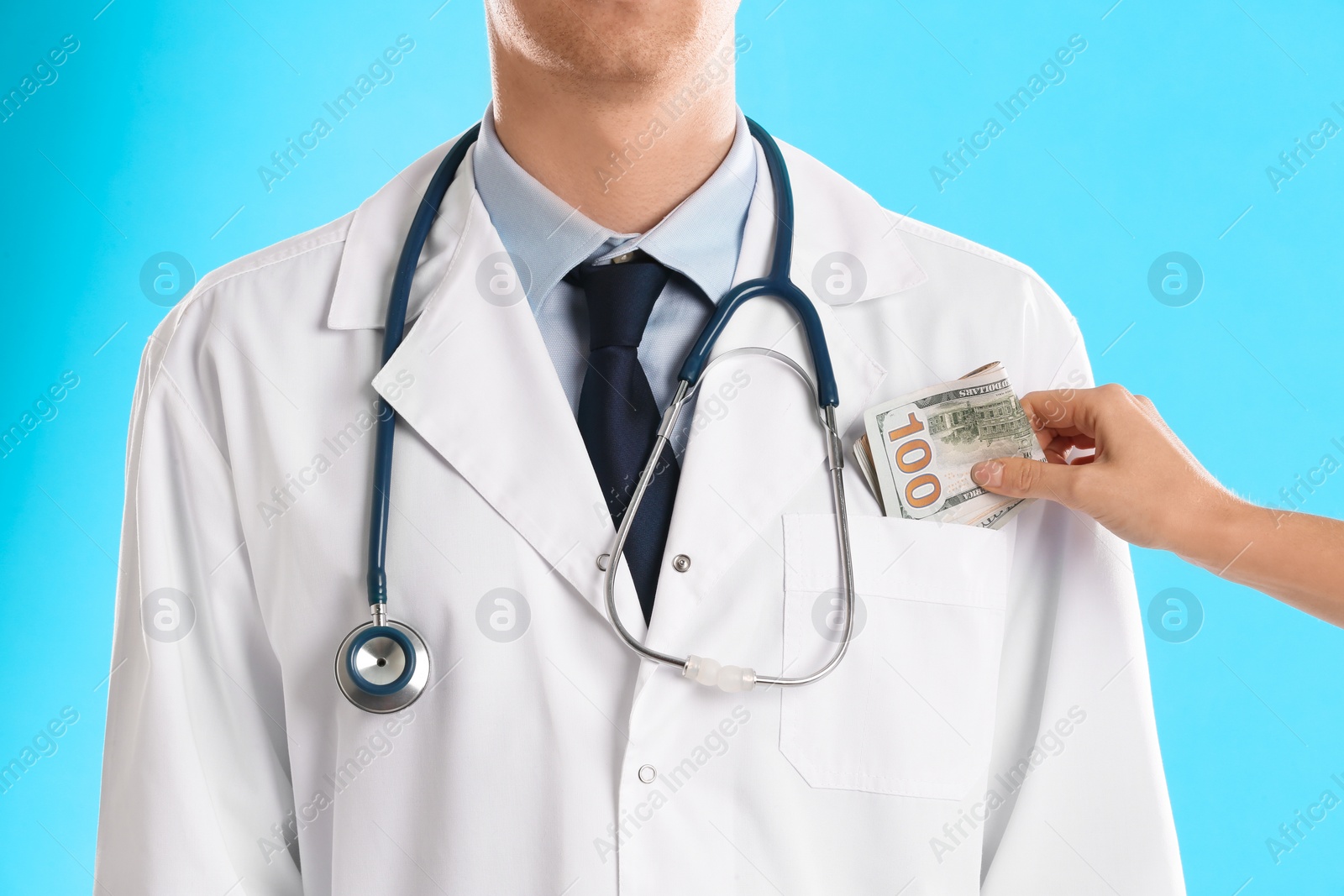 Photo of Patient putting bribe into doctor's pocket on light blue background, closeup. Corruption in medicine