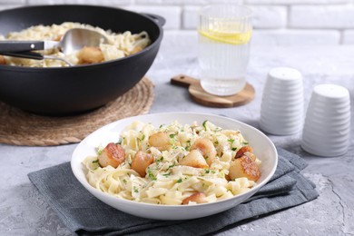 Photo of Delicious scallop pasta with spices in bowl on gray textured table