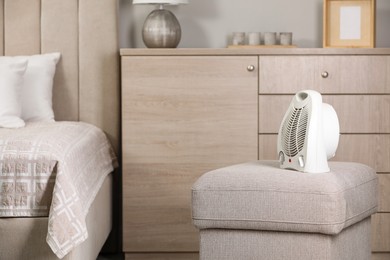 Modern electric fan heater on pouf in cozy room