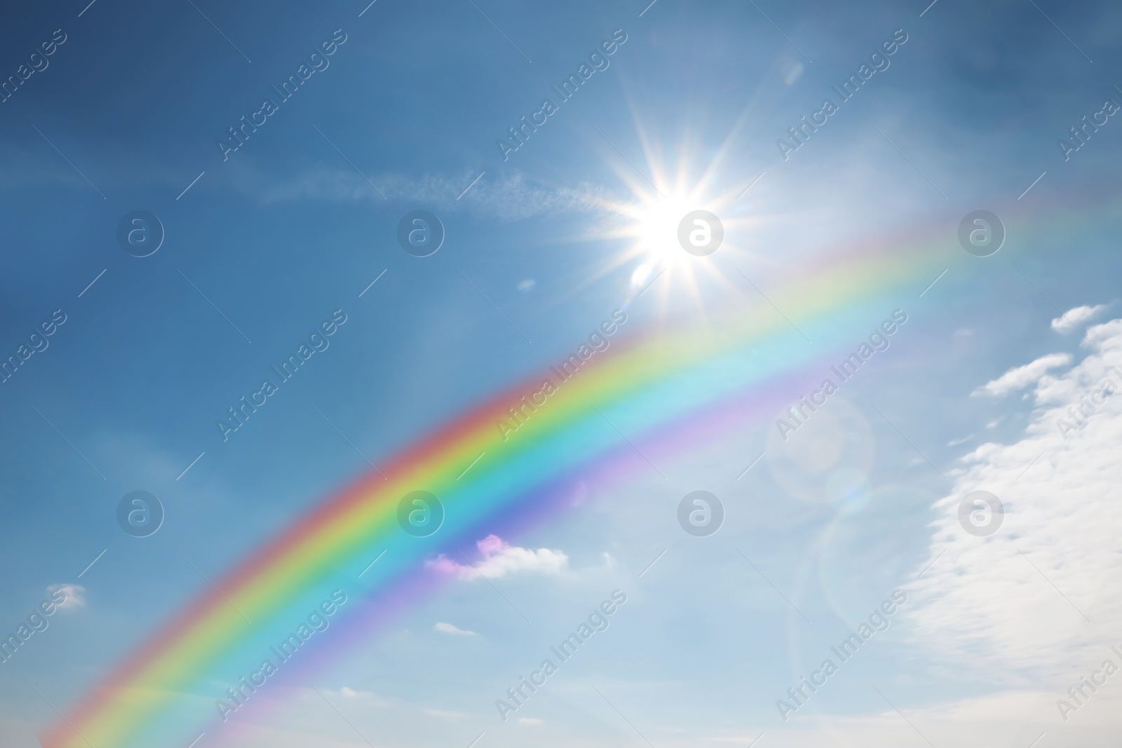 Image of Beautiful rainbow in blue sky with white clouds on sunny day