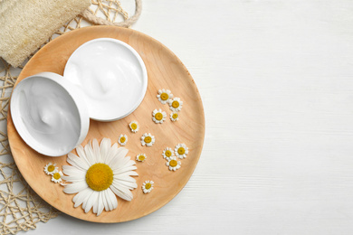 Photo of Jar of cream, chamomiles and loofah on white wooden table, flat lay. Space for text