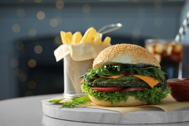 Photo of Tasty vegetarian burger with spinach cutlet, cheese and vegetables on white table against blurred lights, closeup. Space for text