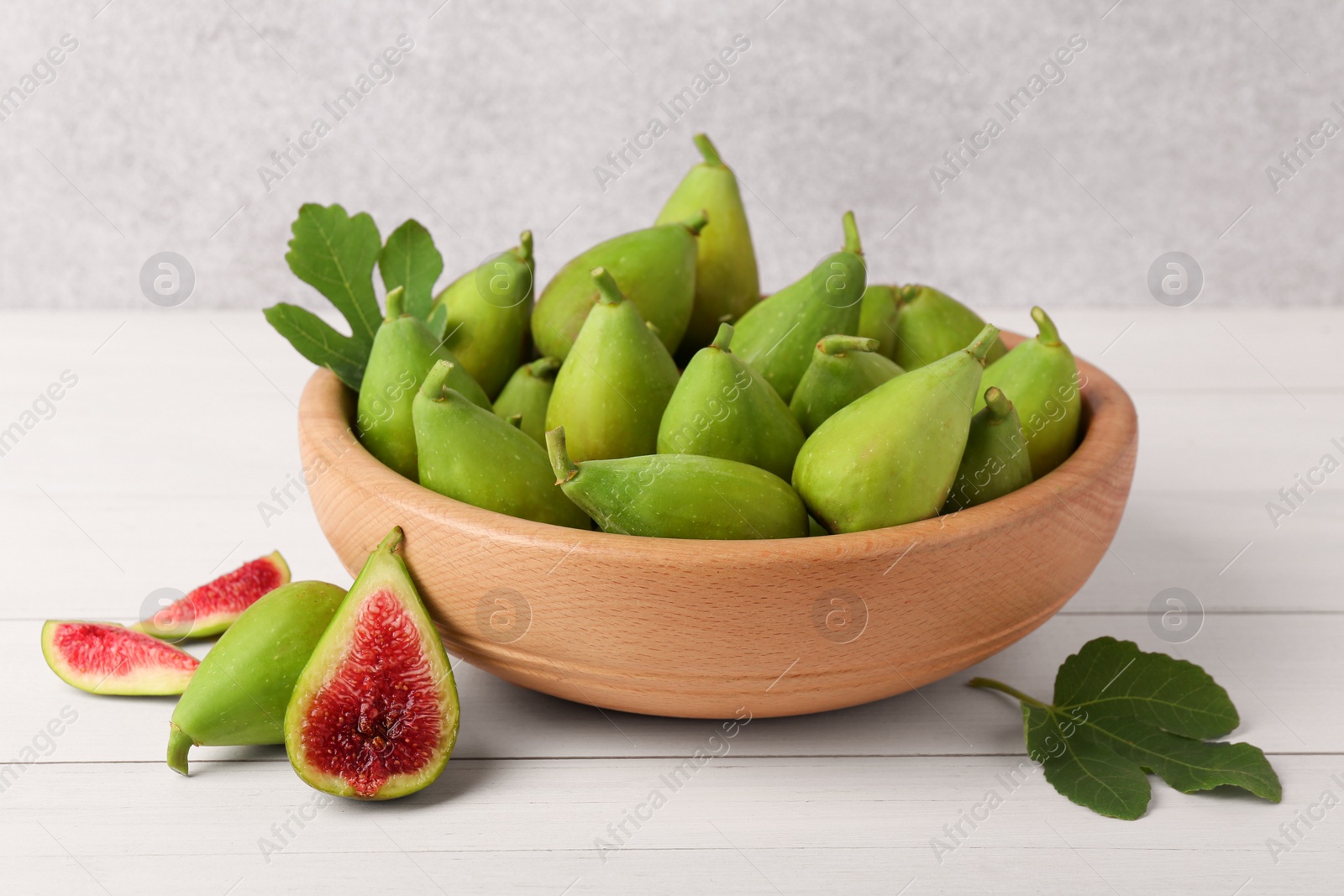 Photo of Cut and whole fresh green figs on white wooden table near grey wall