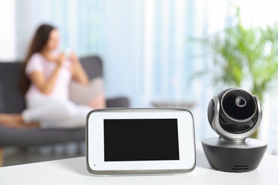 Photo of Baby monitor and camera on table and woman resting in living room. Video nanny