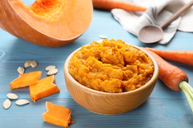 Photo of Bowl with tasty puree, carrots and pumpkin on light blue wooden table