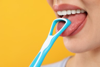 Woman brushing her tongue with cleaner on yellow background, closeup. Space for text