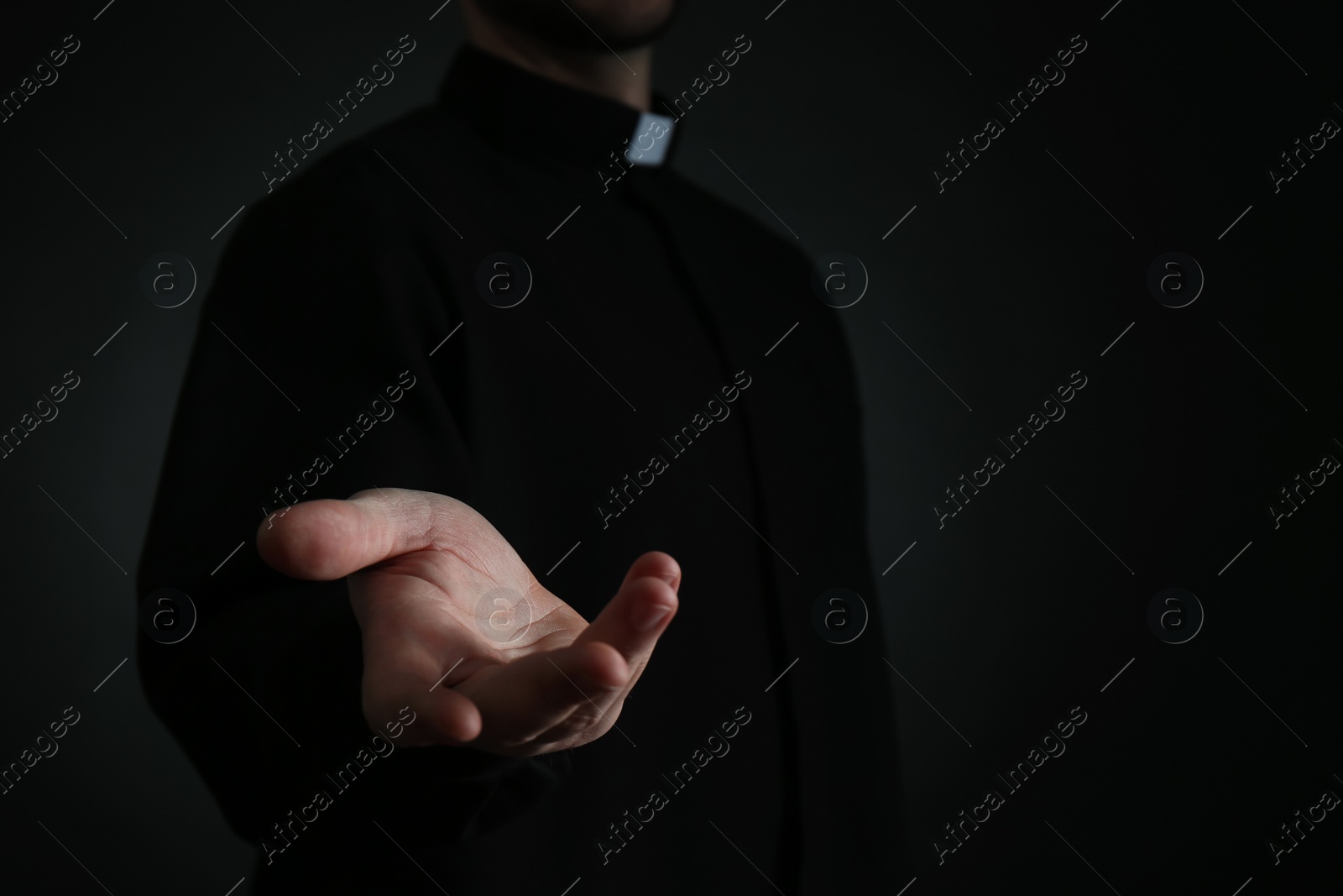 Photo of Priest reaching out his hand on dark background, closeup. Space for text