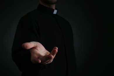Priest reaching out his hand on dark background, closeup. Space for text