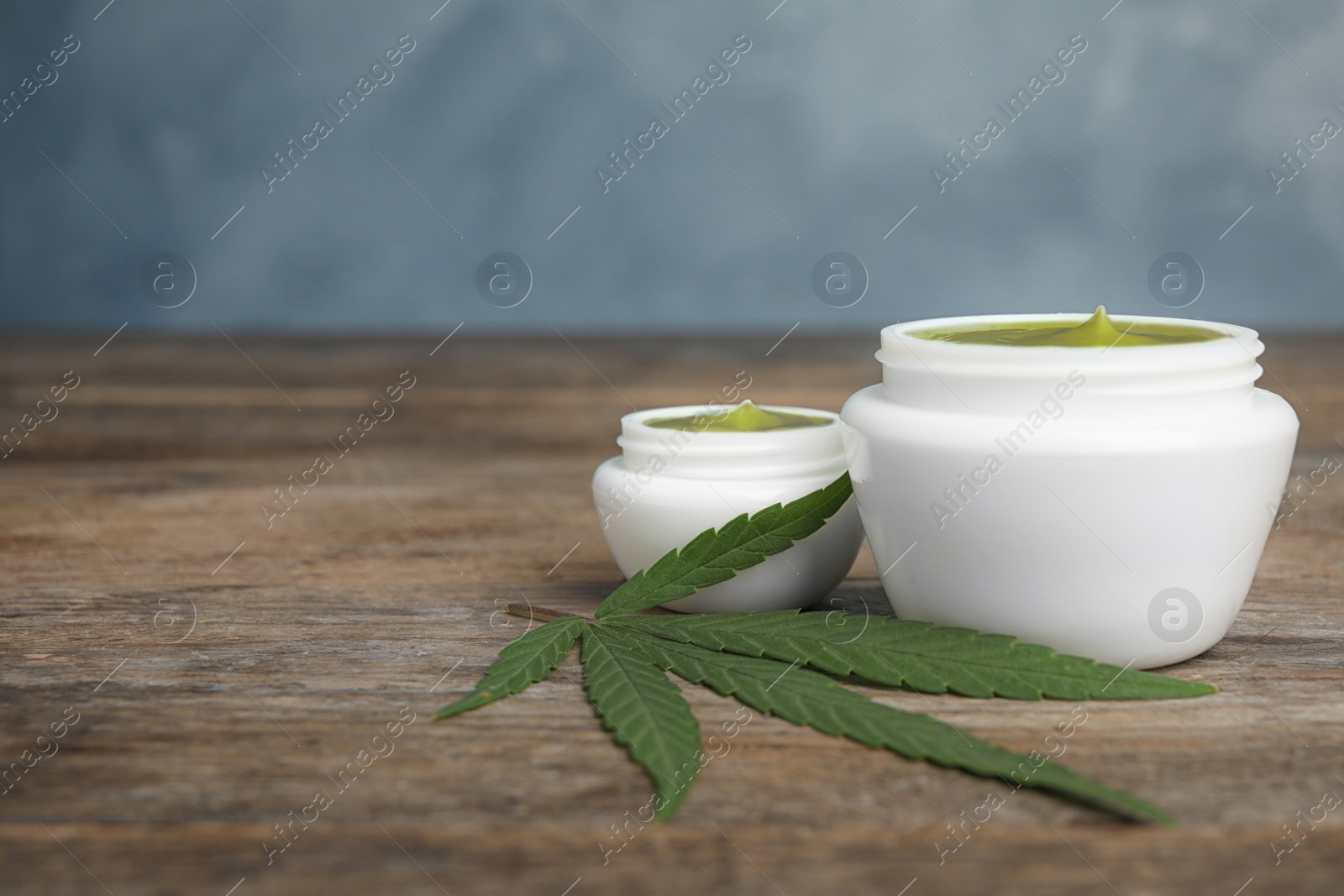 Photo of Jars of hemp cream on wooden table against blue background, space for text. Organic cosmetics