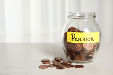 Photo of Glass jar with label PENSION and coins on white table. Space for text