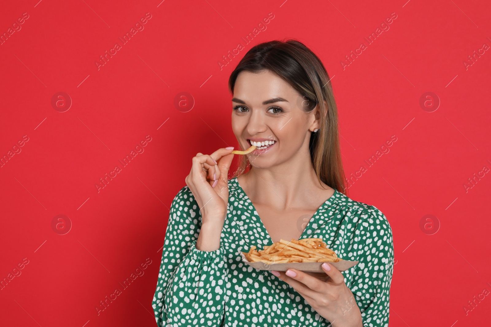 Photo of Young woman eating French fries on red background