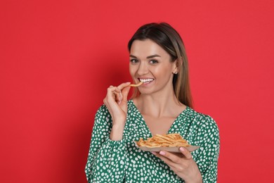 Young woman eating French fries on red background