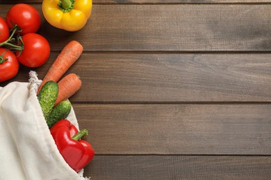 Photo of Cloth bag with fresh vegetables on wooden table, flat lay. Space for text