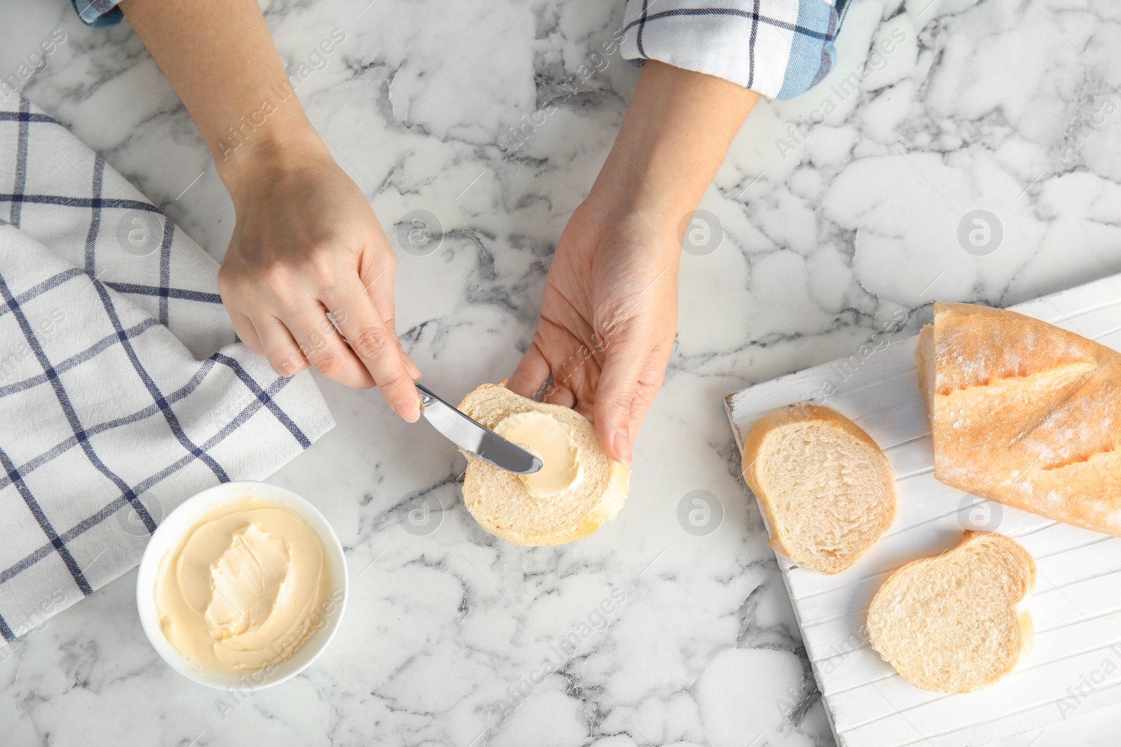 Photo of Woman spreading butter onto bread over marble table, top view