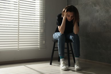 Photo of Sad young woman sitting on chair at home, space for text