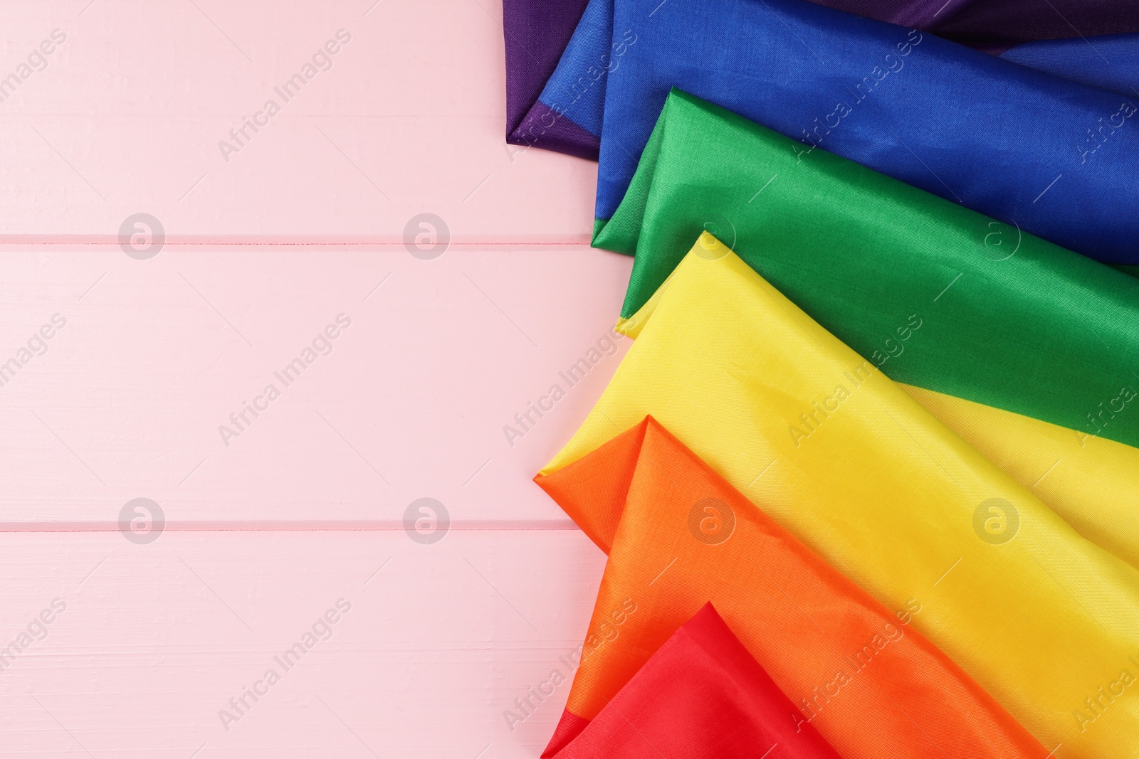 Photo of Rainbow LGBT flag on pink wooden table, top view. Space for text