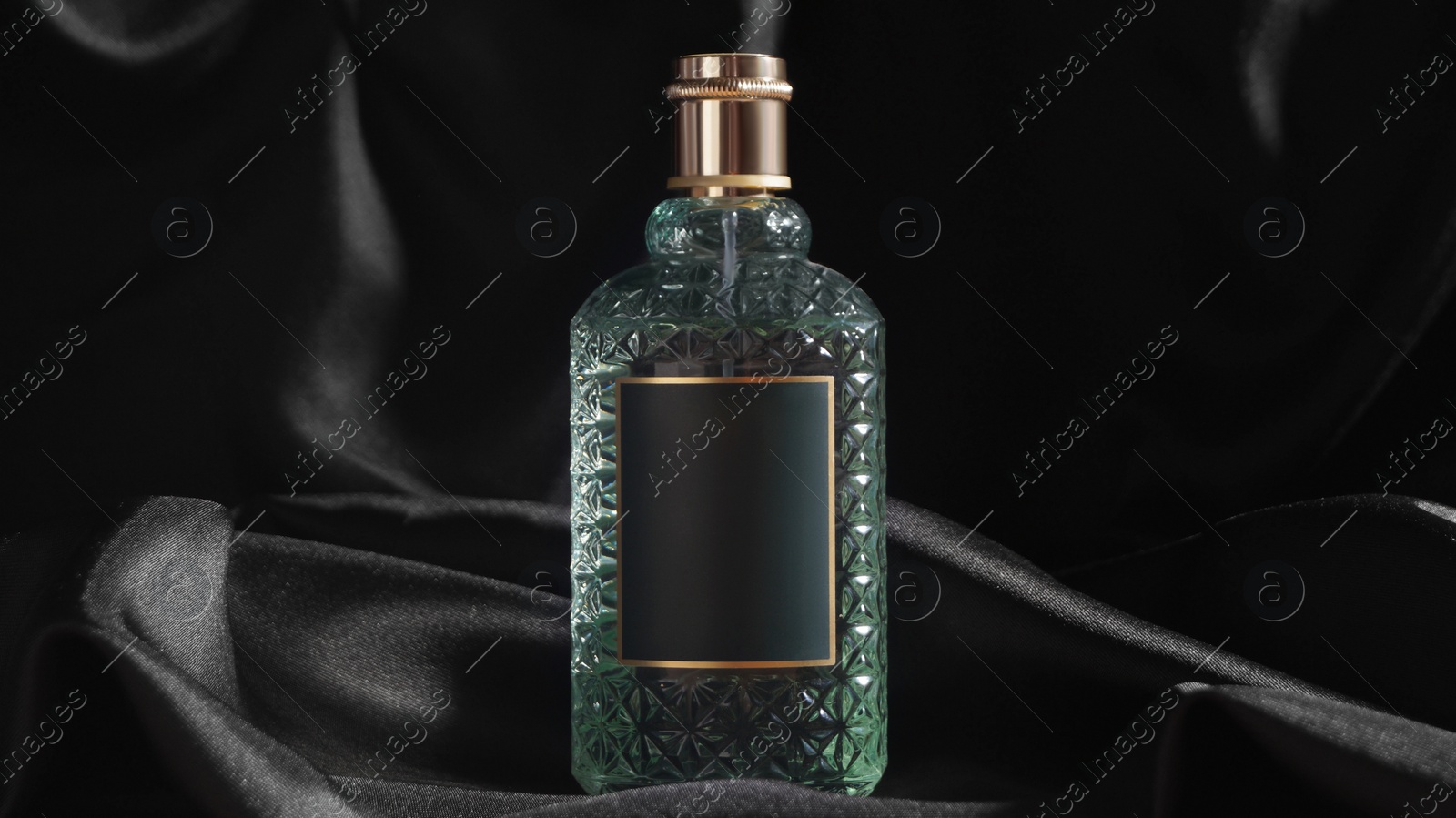 Photo of Luxury bottle of perfume on black silk, closeup