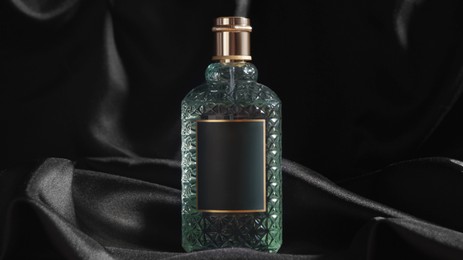 Photo of Luxury bottle of perfume on black silk, closeup