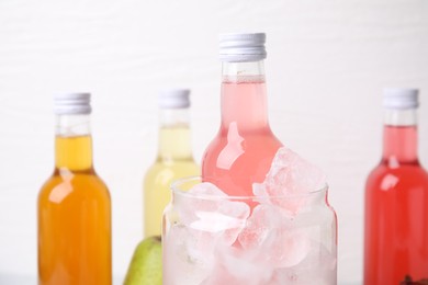 Photo of Tasty kombucha in bottles and glass with ice on white background, closeup