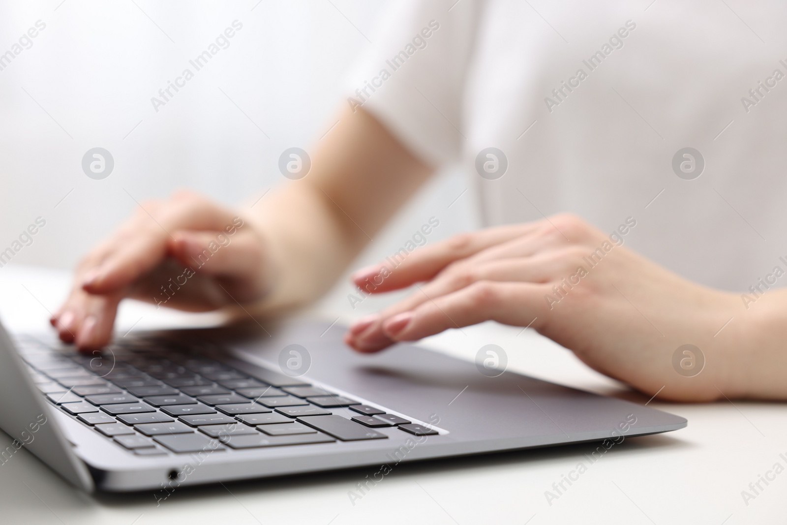 Photo of E-learning. Woman using laptop at white table indoors, closeup