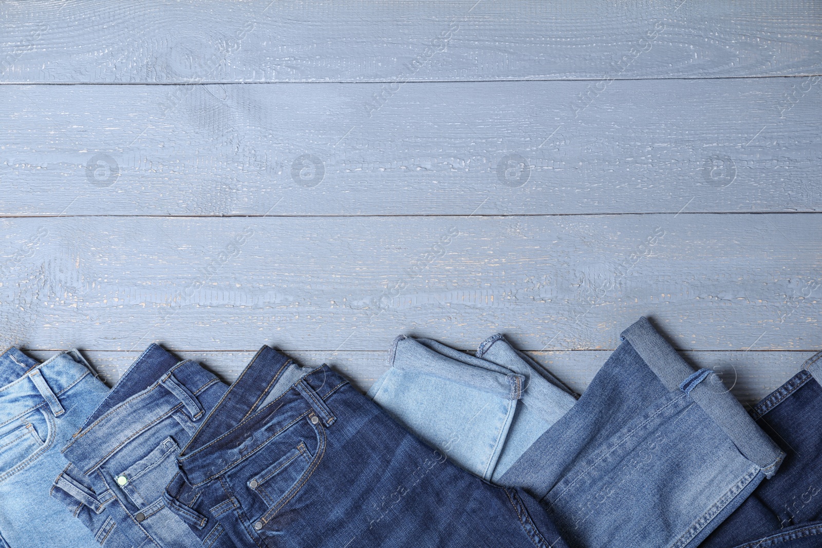 Photo of Collection of stylish jeans on grey wooden background, flat lay. Space for text