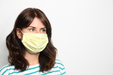 Young woman in protective face mask on light background, space for text