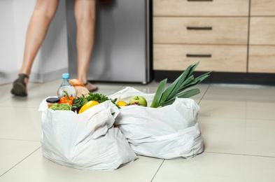 Photo of Plastic bags with vegetables on floor and young woman in kitchen