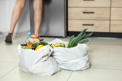 Plastic bags with vegetables on floor and young woman in kitchen