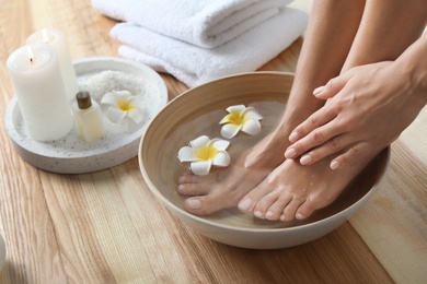 Photo of Closeup view of woman soaking her feet in dish with water and flowers on wooden floor. Spa treatment
