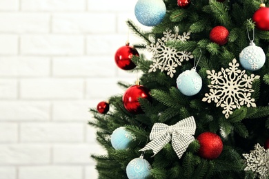 Photo of Beautiful Christmas tree with decor against brick wall. Space for text