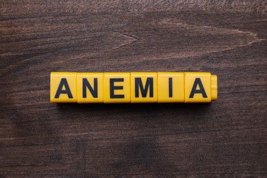 Word Anemia made with yellow cubes on wooden table, flat lay