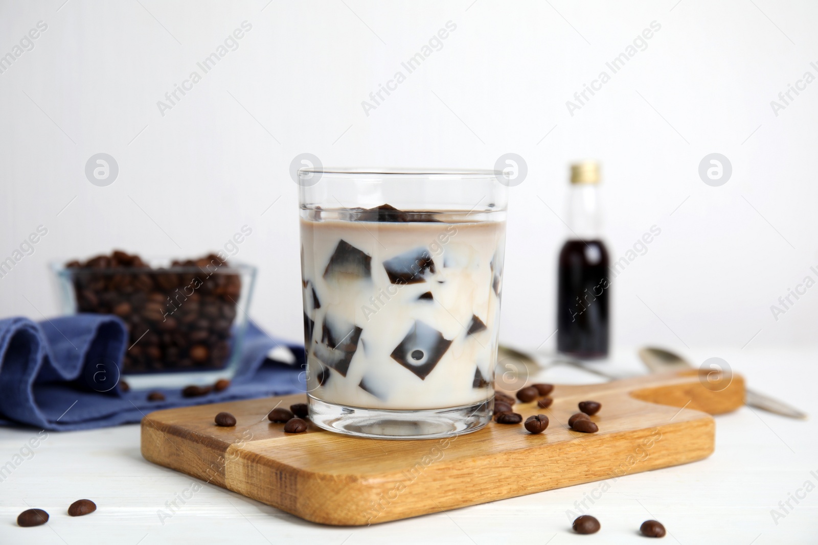 Photo of Glass of milk with grass jelly and coffee beans on white wooden table