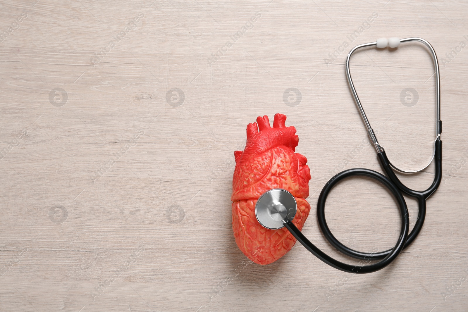 Photo of Stethoscope, heart model and space for text on wooden background, flat lay. Cardiology concept