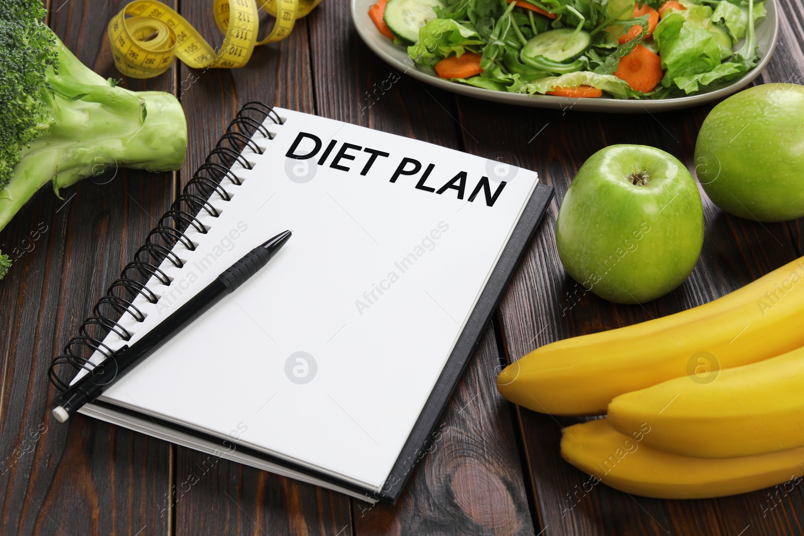 Photo of Notebook with phrase Diet Plan, measuring tape and different products on wooden table. Weight loss concept