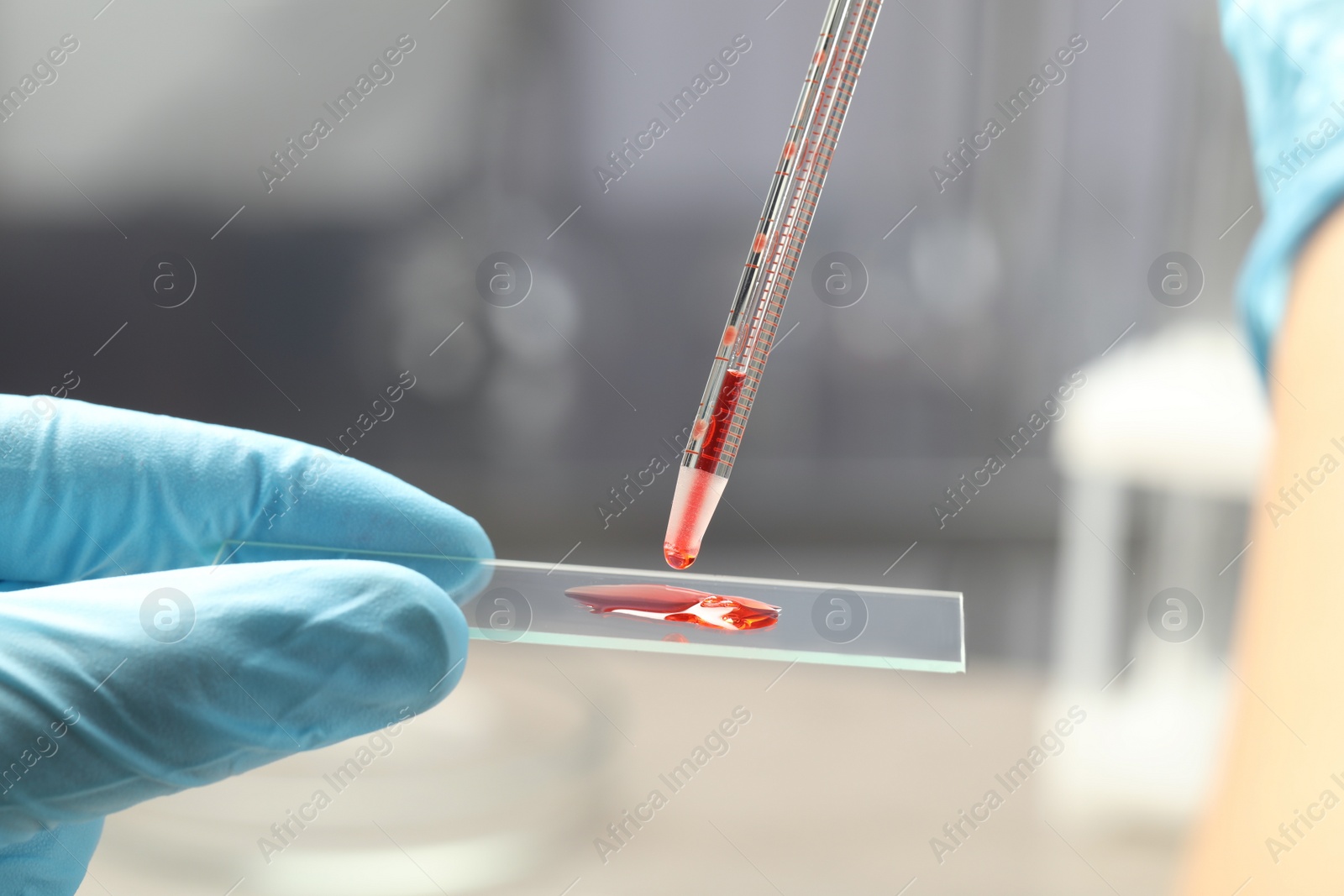 Photo of Scientist dripping sample of red liquid onto microscope slide in laboratory, closeup