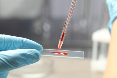 Photo of Scientist dripping sample of red liquid onto microscope slide in laboratory, closeup