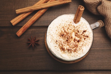 Photo of Cup of hot drink with whipped cream and aromatic cinnamon on wooden table, flat lay