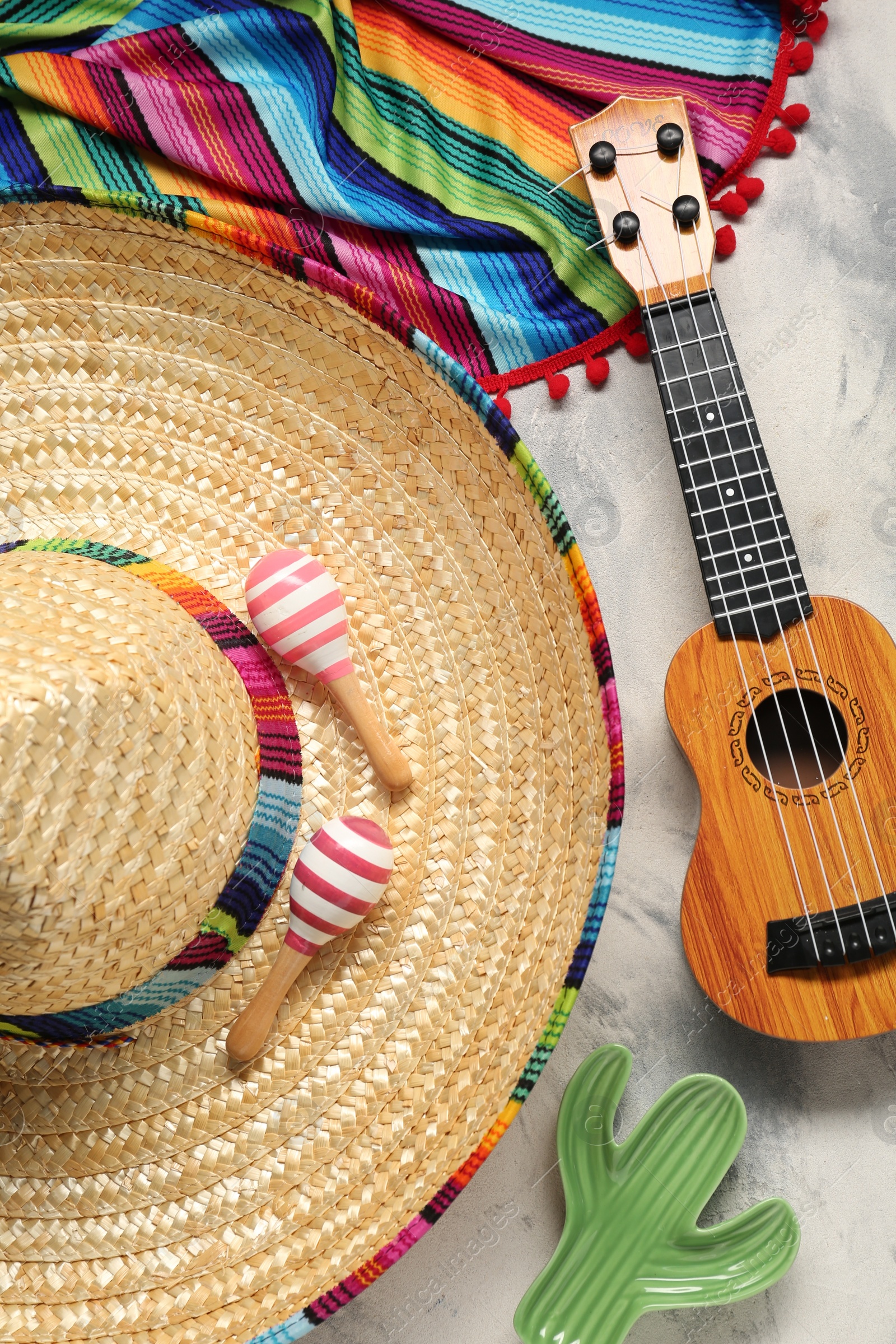 Photo of Mexican sombrero hat, guitar, toy cactus, maracas and colorful poncho on grey textured background, flat lay