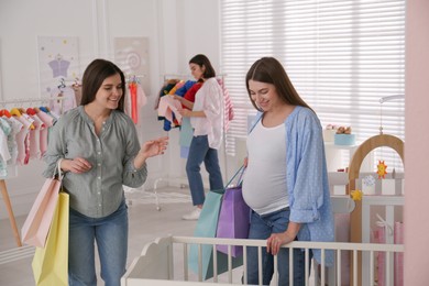 Photo of Happy pregnant women with shopping bags choosing baby crib in store