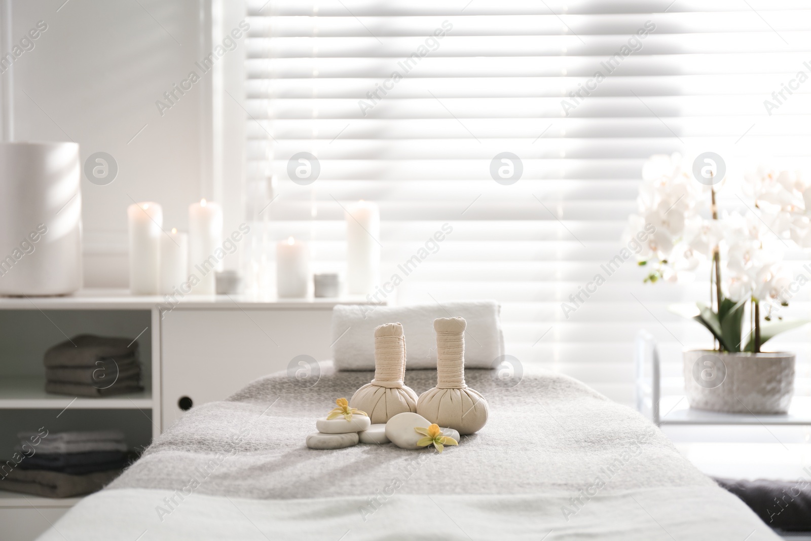 Photo of Herbal bags, orchid flowers and stones on couch in spa salon