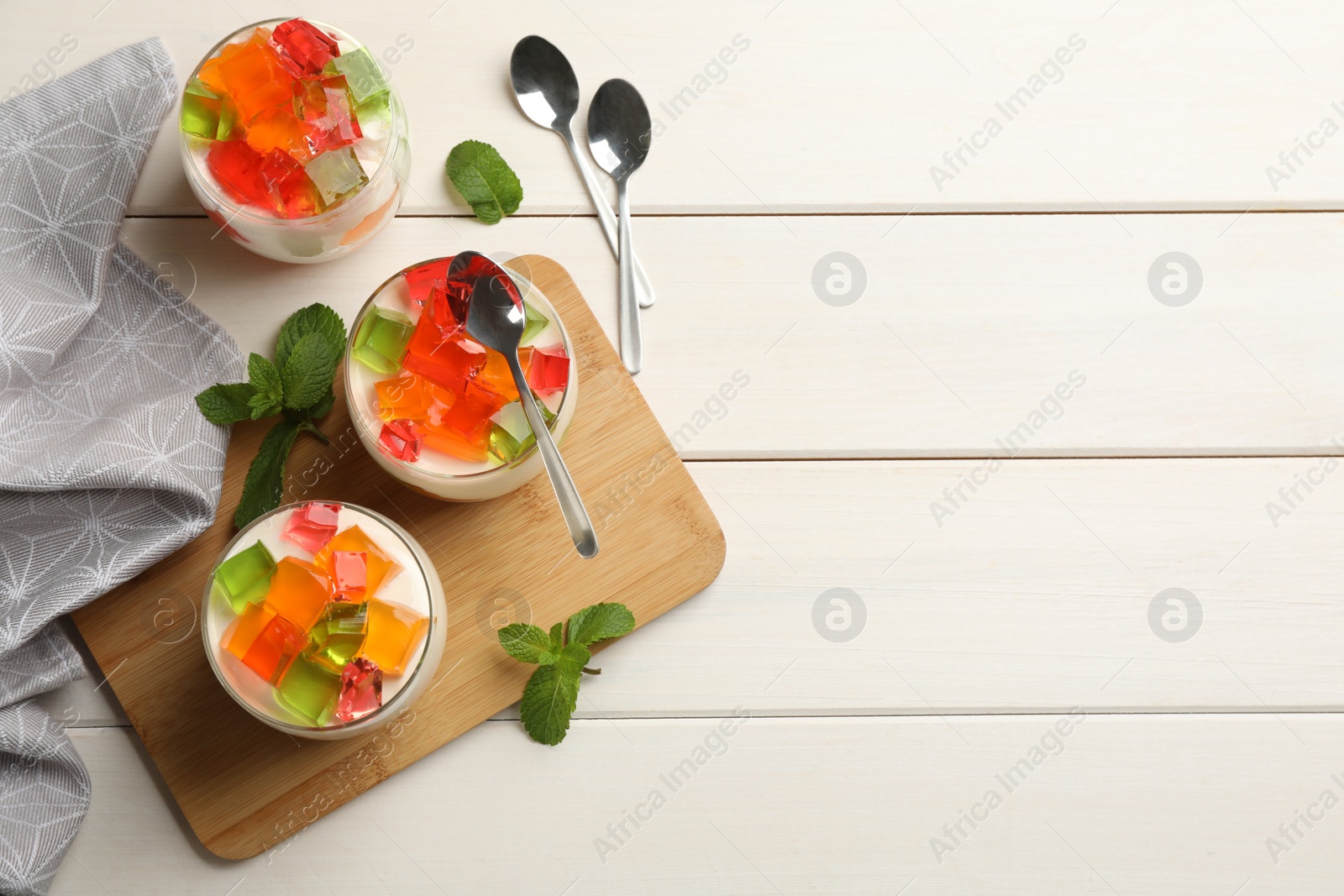 Photo of Delicious broken glass jelly dessert on white wooden table, flat lay. Space for text