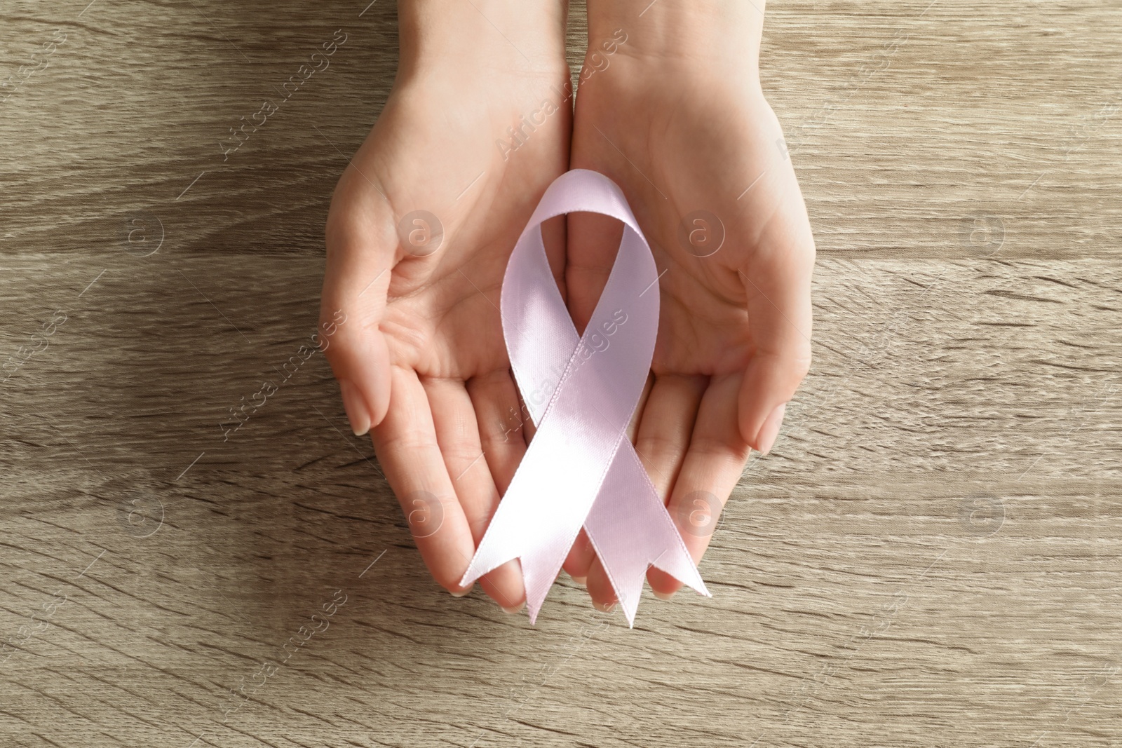 Photo of Woman holding pink ribbon on wooden background, top view. Breast cancer awareness