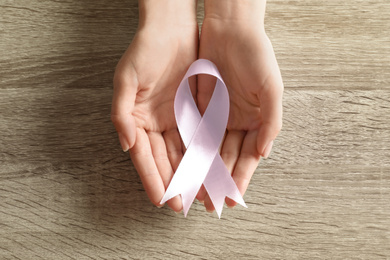 Woman holding pink ribbon on wooden background, top view. Breast cancer awareness