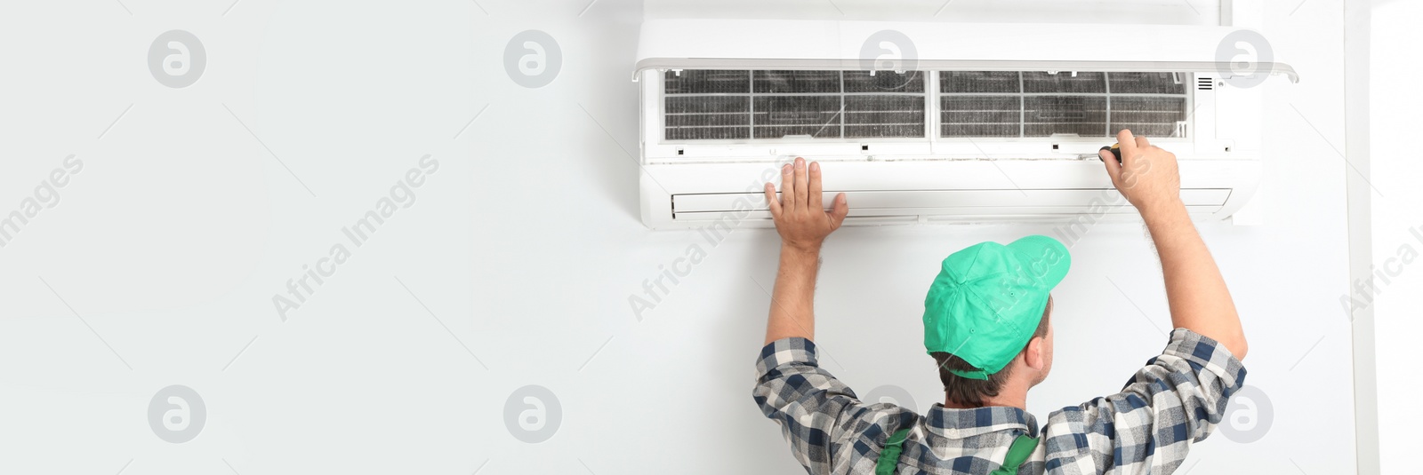 Image of Male technician fixing modern air conditioner indoors, space for text. Banner design