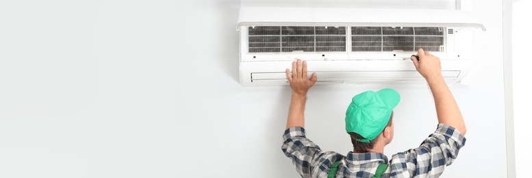 Image of Male technician fixing modern air conditioner indoors, space for text. Banner design