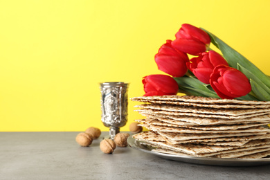 Photo of Passover matzos, goblet, walnuts and tulips on grey table, space for text. Pesach celebration