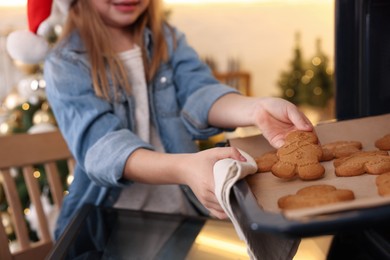 Little child in Santa hat taking baking sheet with Christmas cookies out of oven indoors, closeup