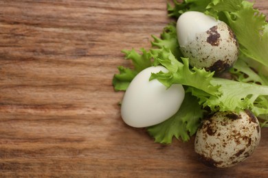 Unpeeled and peeled boiled quail eggs with lettuce on wooden table, flat lay. Space for text