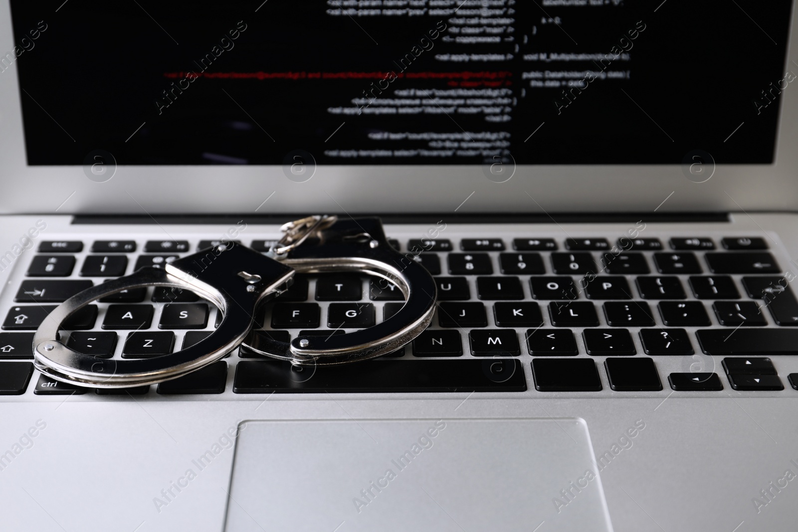 Photo of Handcuffs on modern laptop, closeup. Cyber crime